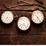 A row of four antique pocket watches on a old wooden table.